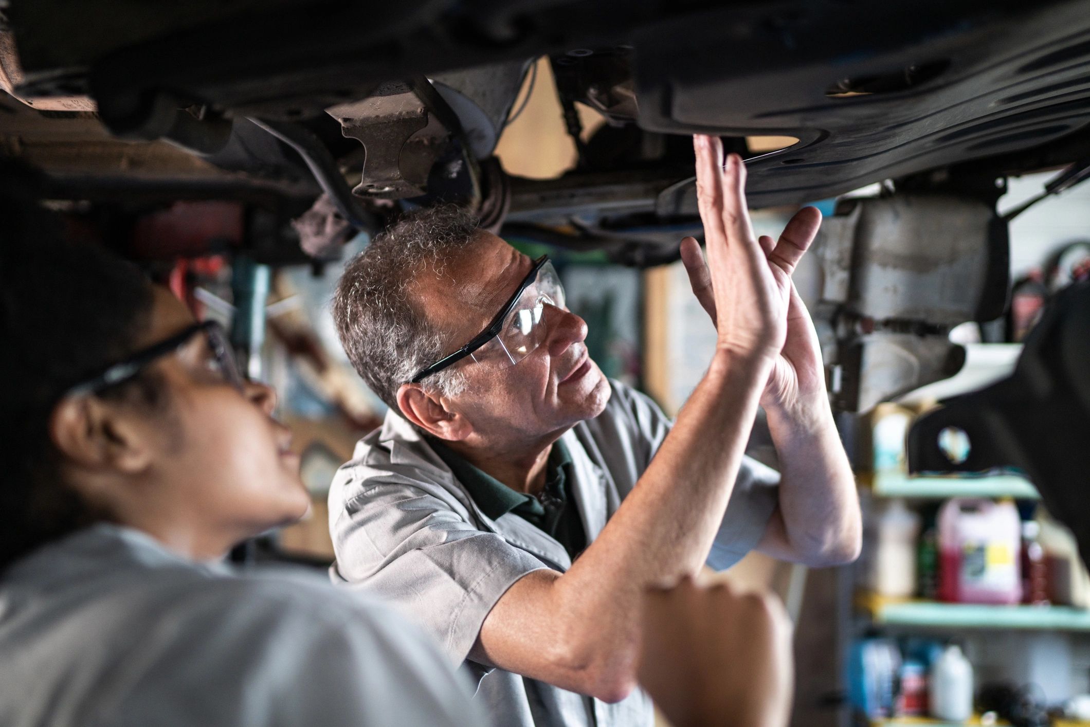 Auto mechanic teaching an assistant in a repair shop